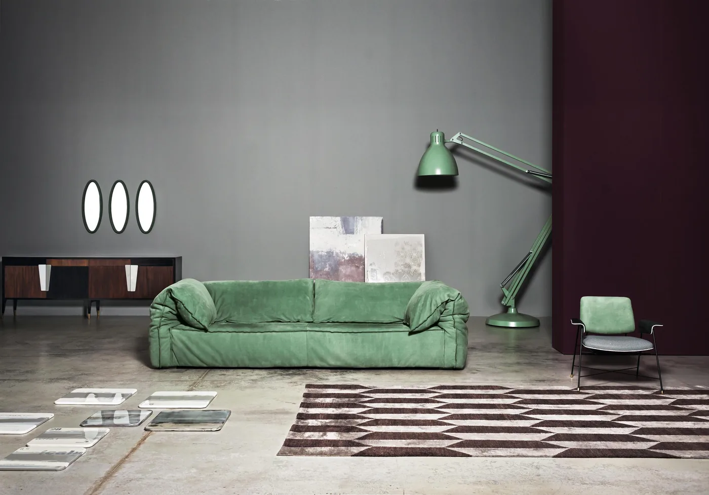 A green sofa with a softly folded surface and low arms against a dark wall.