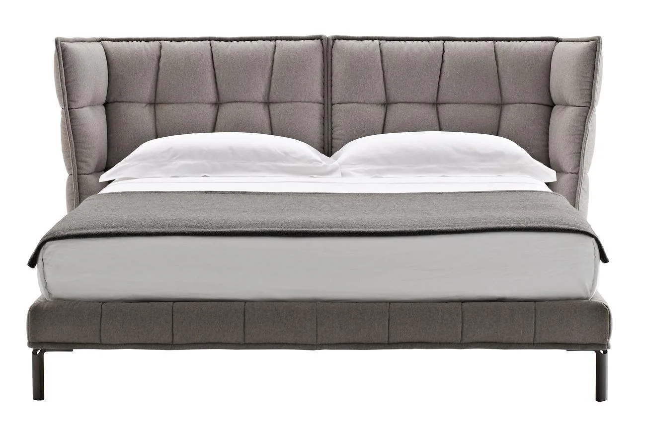 A grey upholstered bed with a tall padded headboard on a white background.