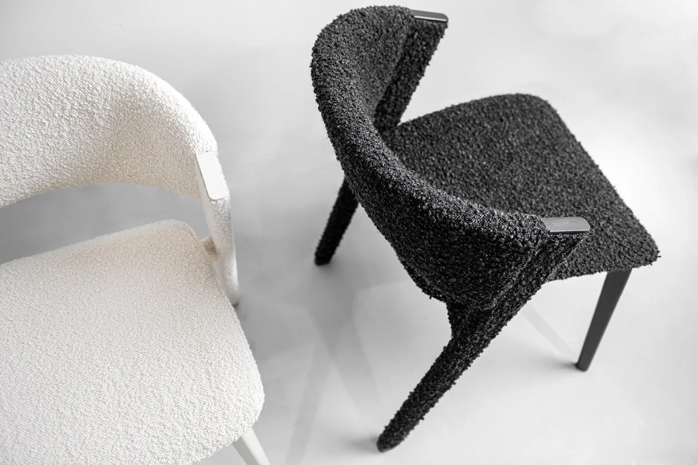 Pale and dark textured lounge chairs with open arm profiles and slim legs.