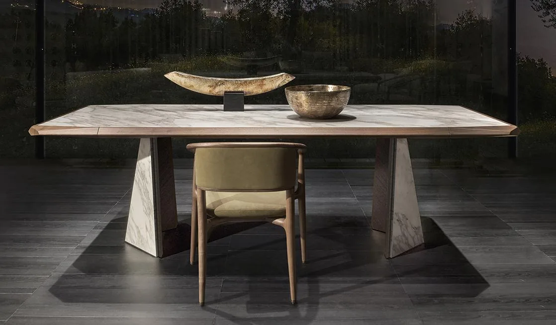 A rectangular dining table with two broad sculptural supports and a chair viewed from the front.