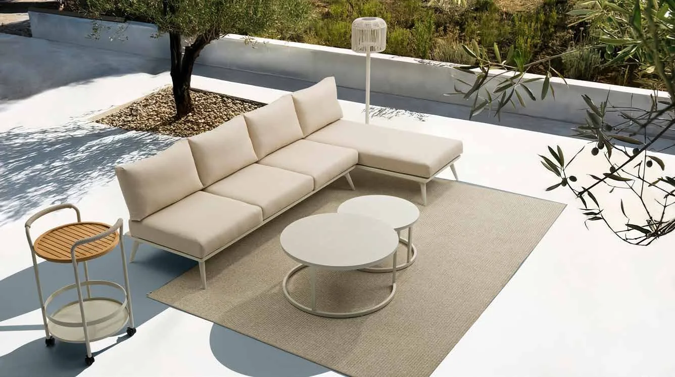 A light-coloured modular outdoor sofa with loose cushions arranged around a patio table.